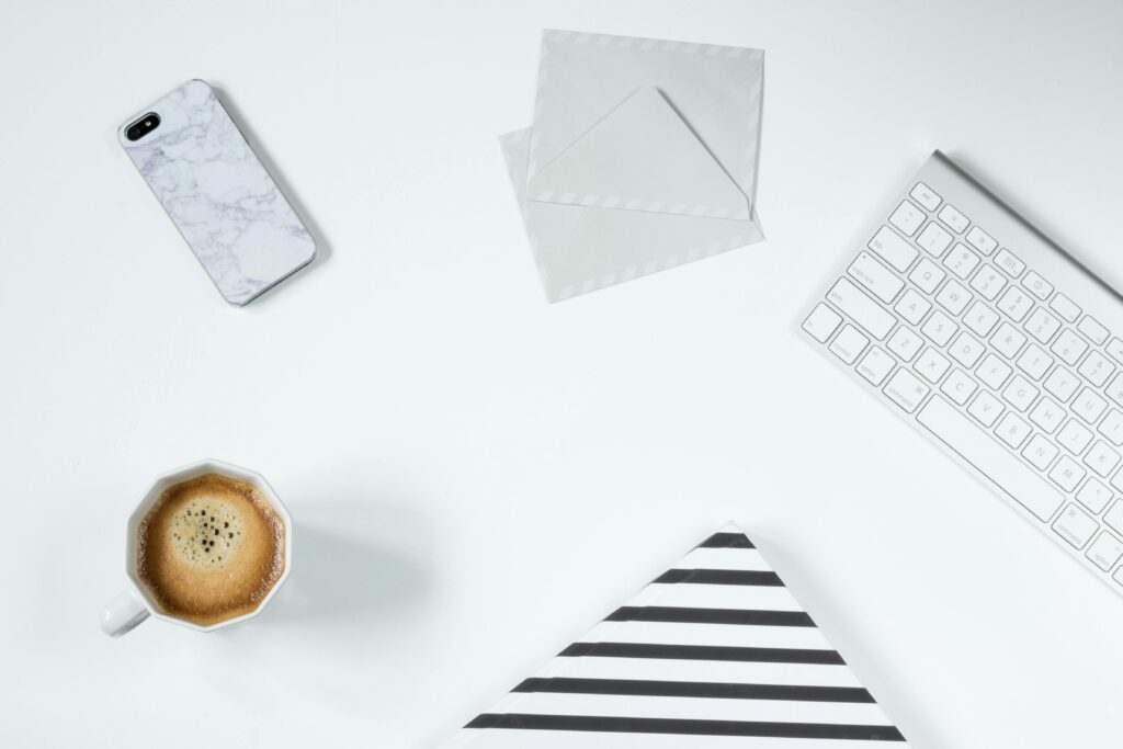 Clean minimalist workspace featuring coffee, keyboard, phone, and envelopes on a white desk.